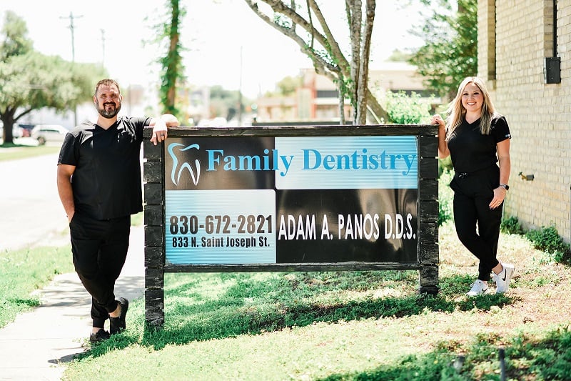 Dr. Panos and Lexi Panos standing outside of building posing with office sign